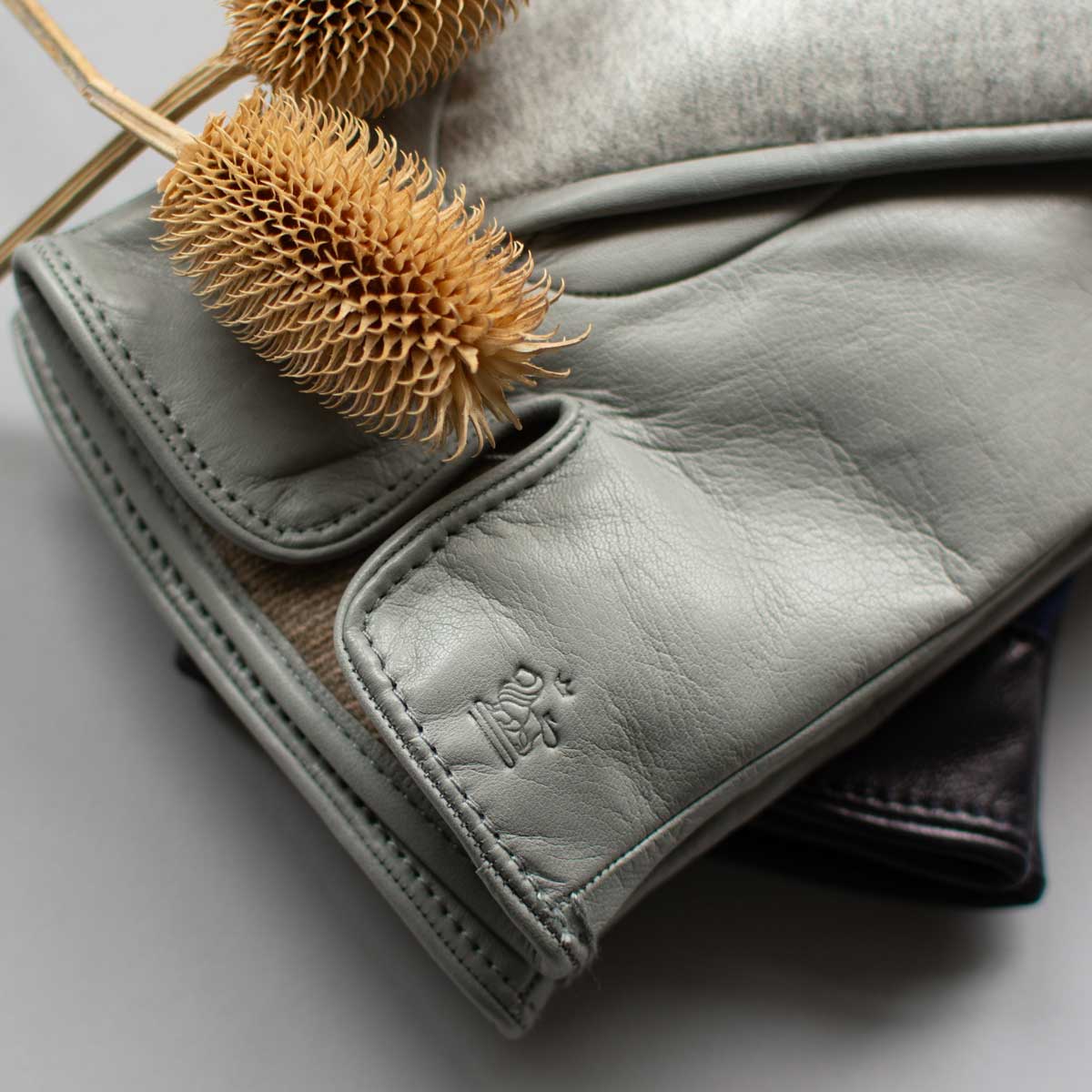 Gray leather glove with a dried teasel head on a light gray background