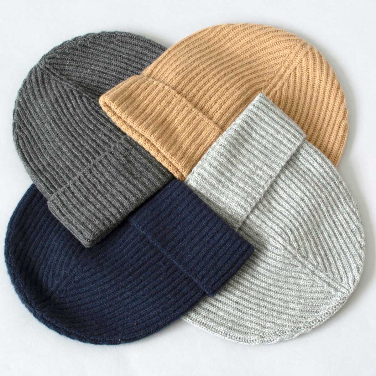 Four cashmere beanie hats in grey, beige, navy, and light grey on a white background