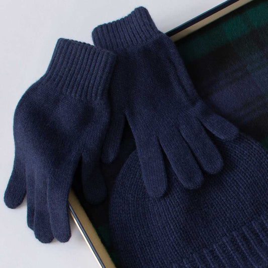 Pair of dark blue gloves pictured with a hat and scarf on a white background
